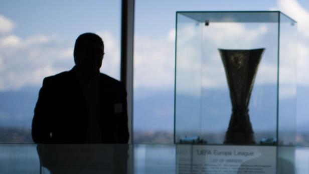 Die UEFA Europa League Trophäe in einer Vitrine, daneben eine Person im Anzug als Silhouette.