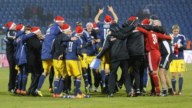 Eine Fußballmannschaft feiert mit Weihnachtsmützen auf dem Spielfeld.