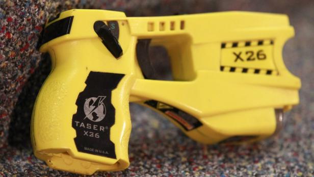 Ein gelber Taser X26 liegt auf einem gemusterten Untergrund.
