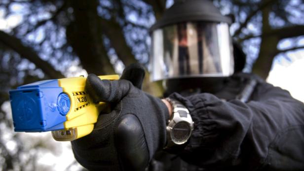Ein Polizist in Schutzkleidung zielt mit einem gelben Taser X26.