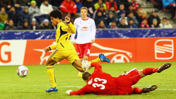 Ein Fußballspieler in Gelb schießt auf das Tor, während der Torwart in Rot versucht, den Ball abzuwehren.