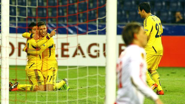 Zwei Fußballspieler in gelben Trikots umarmen sich kniend vor einem Tornetz.