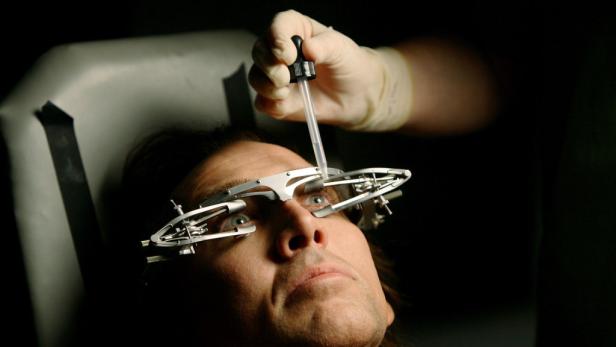 Einem Mann werden Augentropfen verabreicht, während er eine spezielle Brille trägt.