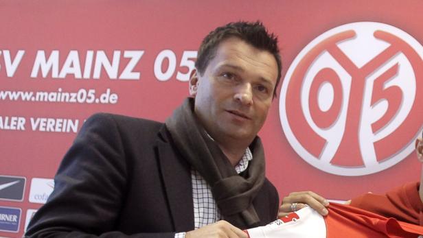Ein Mann mit Schal hält ein Trikot des 1. FSV Mainz 05 in der Hand.