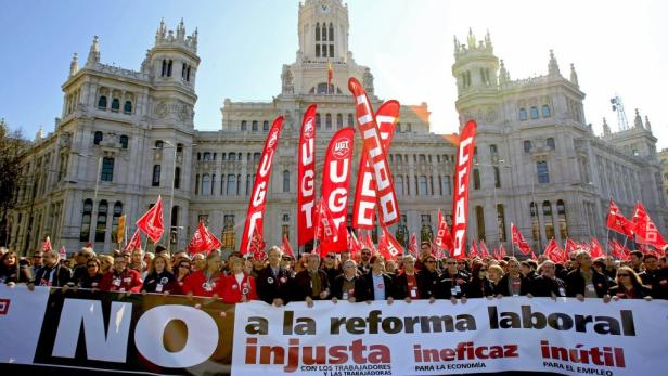 Eine Menschenmenge demonstriert mit roten Fahnen und einem Banner gegen eine Arbeitsmarktreform in Madrid.
