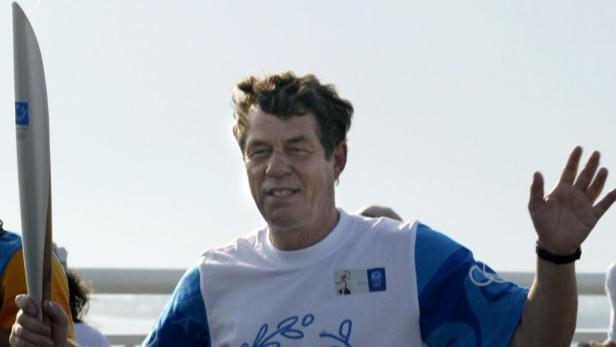 Ein Mann trägt die olympische Fackel und winkt.