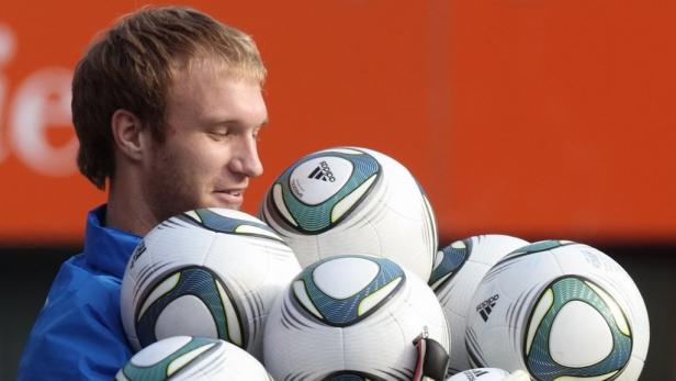 Ein Mann hält mehrere Fußbälle der Marke Adidas.