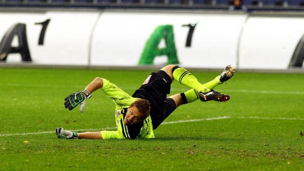 Ein Torwart liegt auf dem Rasen und versucht, einen Ball zu halten.