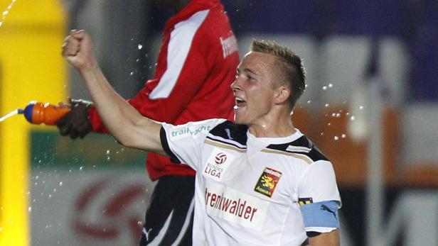 Ein jubelnder Fußballspieler wird mit Wasser bespritzt.