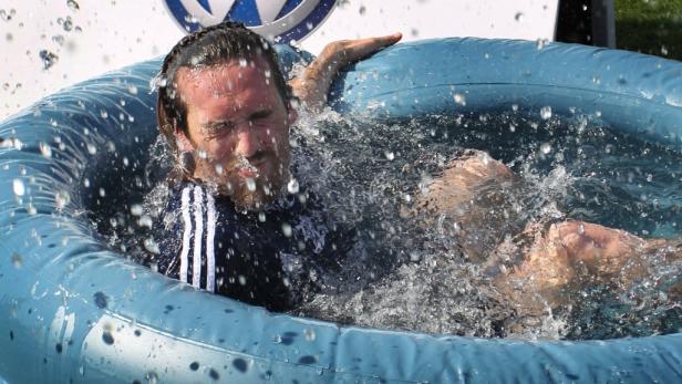 Ein Mann liegt in einem blauen Planschbecken, umgeben von spritzendem Wasser.