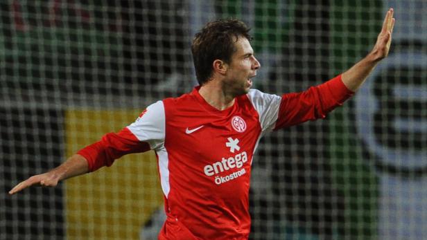 Ein Fußballspieler im roten Trikot jubelt mit erhobenem Arm.