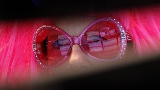 Nahaufnahme einer Person mit pinkfarbener Perücke und übergroßer, rosafarbener Sonnenbrille.