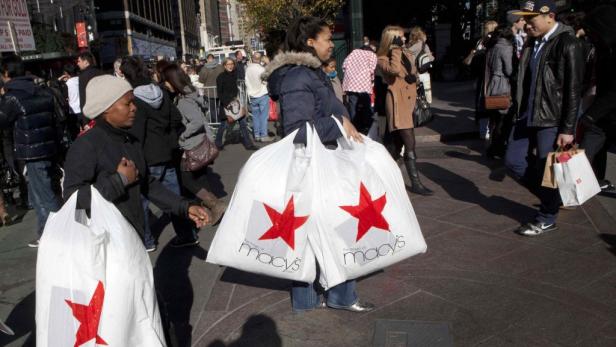 Menschen mit Einkaufstüten von Macy's auf einer belebten Straße.