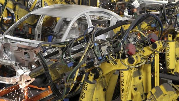 Gelbe Roboter schweißen eine Karosserie in einer Fabrik.