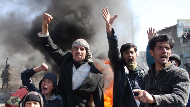 Eine Gruppe von Menschen demonstriert vor einem Hintergrund aus Rauch und Feuer.