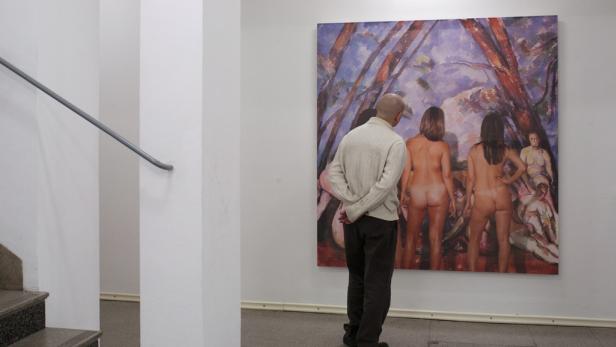 Ein Mann betrachtet in einer Galerie ein Gemälde von mehreren Aktdarstellungen.