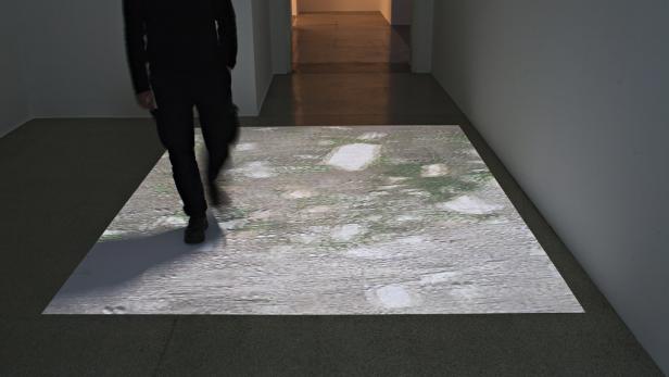 Eine Person geht in einem Ausstellungsraum über eine Projektion eines Weges.