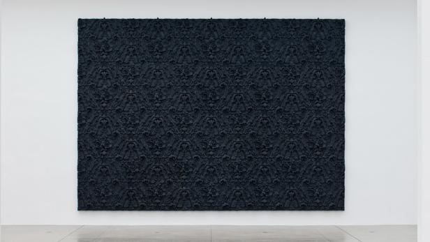 Ein großes, schwarzes Relief mit einem floralen Muster hängt an einer weißen Wand.