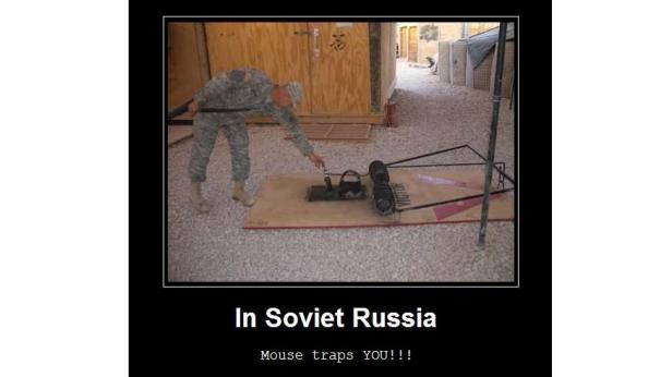 Ein Soldat in Tarnkleidung manipuliert eine übergroße Mausefalle.