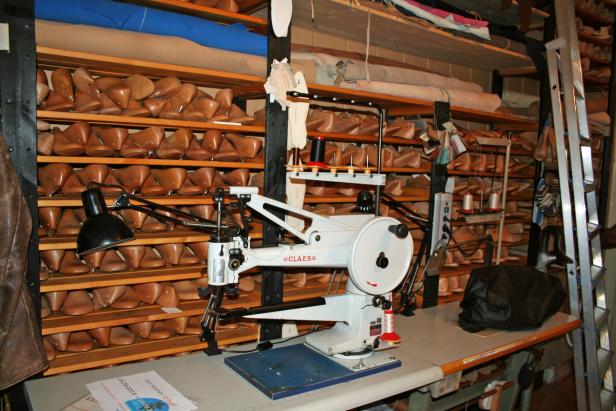 Eine Claes-Nähmaschine steht vor Regalen voller Schuhleisten in einer Werkstatt.
