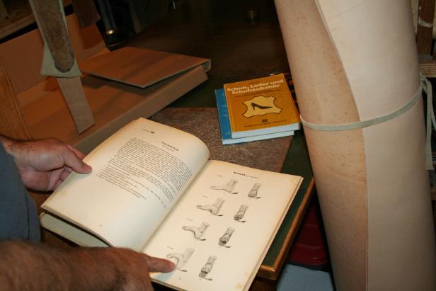 Ein Mann studiert ein Buch über Schuh-, Leder- und Schuhzubehör, das Abbildungen von Fußdeformitäten zeigt.