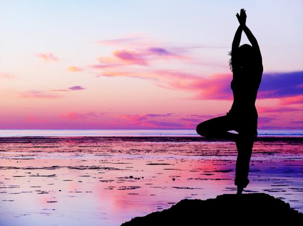Eine Frau macht Yoga am Strand bei Sonnenuntergang.
