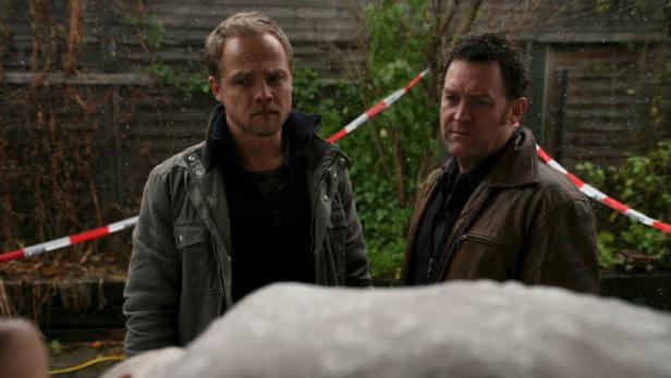 Zwei Männer stehen an einem Tatort mit rot-weißem Absperrband.