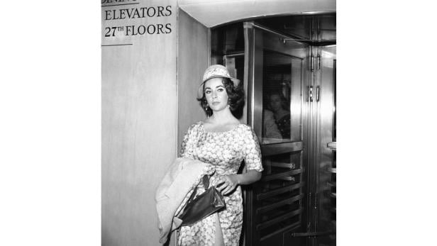 Elizabeth Taylor verlässt einen Aufzug in einem gemusterten Kleid und Hut.
