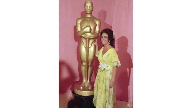 Elizabeth Taylor posiert neben einer Oscar-Statue.