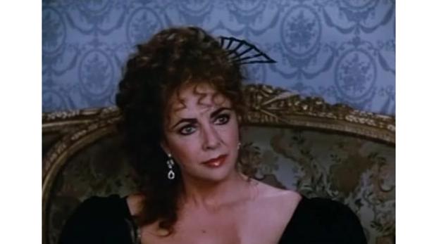 Elizabeth Taylor in einem schwarzen Kleid mit Ohrringen und einem Fächer im Haar.