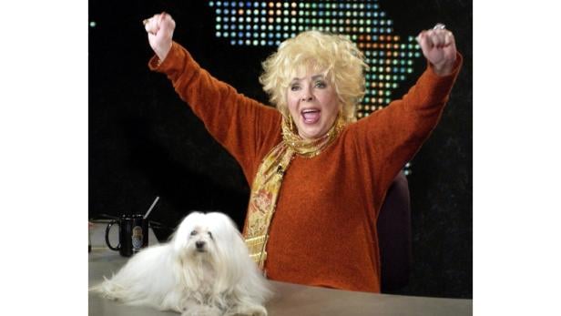 Doris Roberts mit erhobenen Fäusten und einem Malteserhund auf einem Tisch.