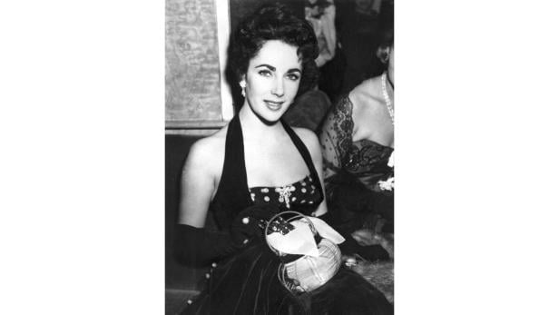 Elizabeth Taylor in einem eleganten, dunklen Kleid mit Handtasche.