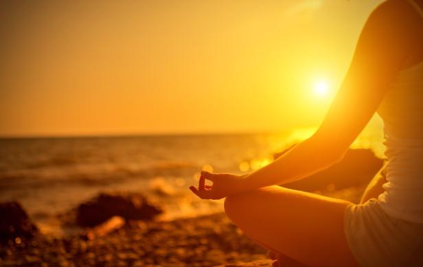 Eine Frau meditiert am Strand bei Sonnenuntergang.