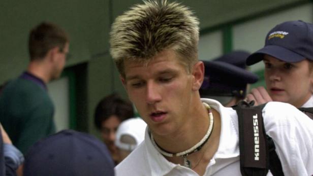 Ein junger Mann mit blond gesträhnten Haaren und Halskette.
