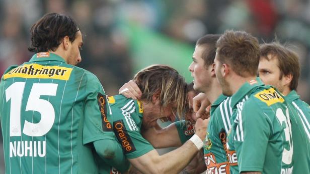 Eine Gruppe Fußballspieler in grünen Trikots umarmt sich auf dem Spielfeld.