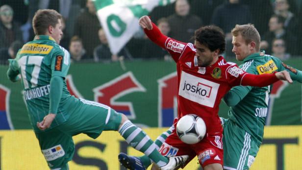 Ein Fußballspieler in Rot kämpft mit zwei Spielern in Grün um den Ball.