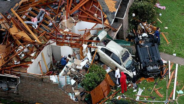 Ein durch einen Tornado zerstörtes Haus mit zwei beschädigten Autos davor.