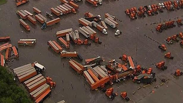 Ein überfluteter Parkplatz mit umgestürzten Lastwagen und Anhängern.