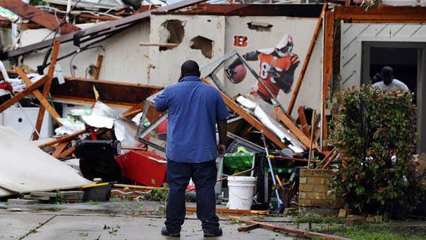 Ein Mann steht vor einem durch einen Tornado beschädigten Haus, auf dessen Wand ein Footballspieler abgebildet ist.