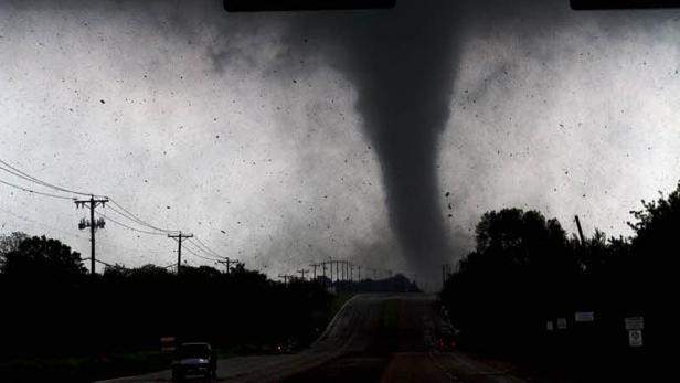 Ein Tornado nähert sich einer Straße, gesäumt von Bäumen und Strommasten.