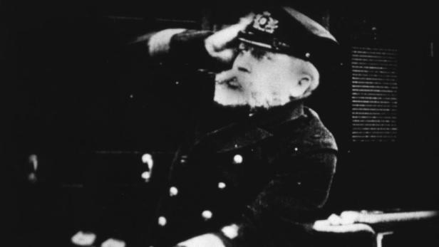 Ein älterer Mann in Uniform und Mütze salutiert.
