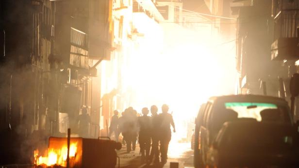 Eine Gruppe von Personen geht eine von Rauch erfüllte Straße entlang, während ein Feuer brennt.