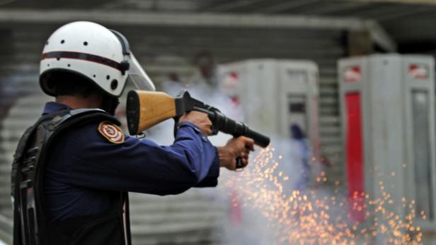 Ein Polizist in Schutzkleidung feuert eine Waffe ab, wobei Funken sprühen.