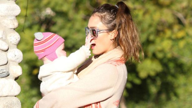 Jessica Alba trägt ihr Baby mit Mütze und streichelt ihr Gesicht.