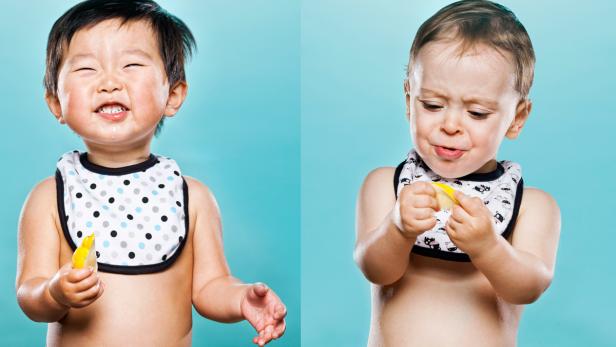 Zwei Babys mit Lätzchen probieren Zitronen vor einem türkisfarbenen Hintergrund.