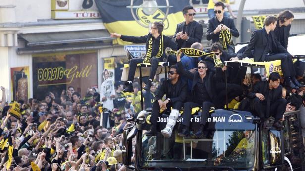 Spieler von Borussia Dortmund feiern auf einem Truck mit Fans im Hintergrund.
