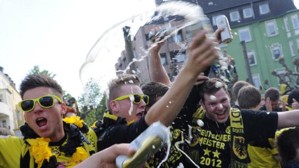 Feiernde Fußballfans von Borussia Dortmund schütten sich mit Bier aus Dosen.