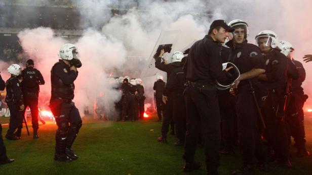 Polizisten stehen inmitten von Rauch und roten Fackeln auf einem grünen Feld.