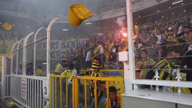Fans zünden Fackeln und werfen Sitze während eines Fußballspiels.