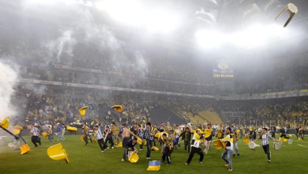 Zuschauer stürmen während eines Fußballspiels den Rasen und werfen Gegenstände.